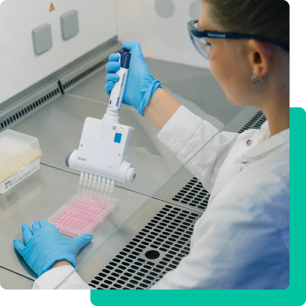 Ein Wissenschaftler, der blaue Handschuhe und eine Schutzbrille trägt, füllt mit einer Mehrkanalpipette Flüssigkeit in eine 96-Well-Platte in einer Labor-Biowanne und unterstützt damit innovative Forschung und pharmazeutische Dienstleistungen.