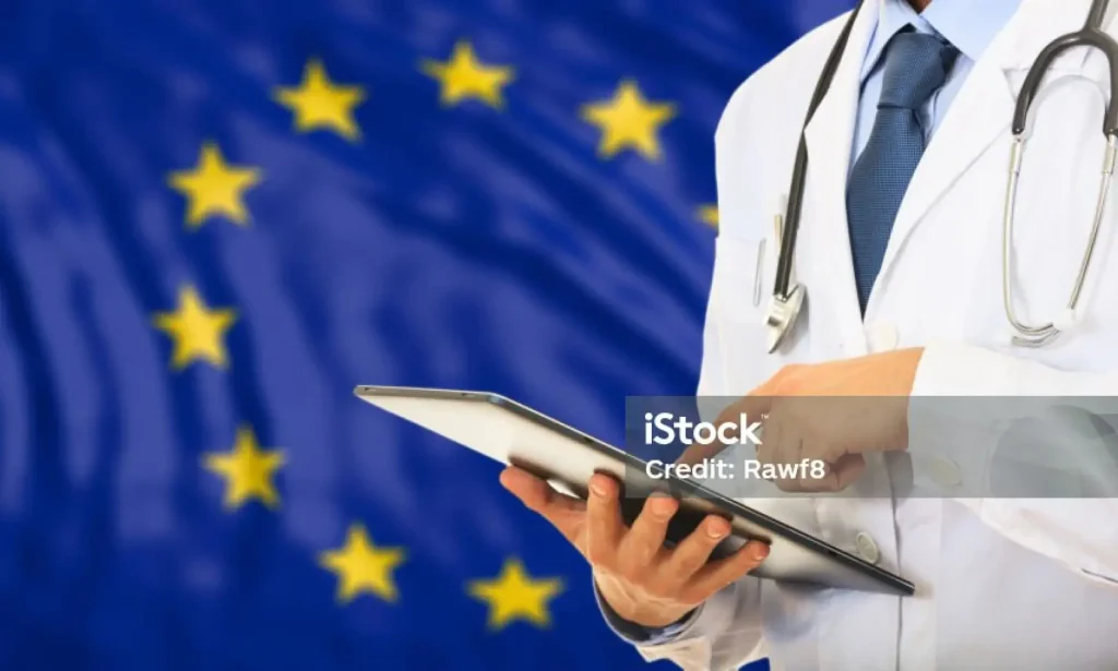 Ein Arzt in einem weißen Kittel mit einem Stethoskop hält ein Tablet in der Hand und steht vor einer Flagge der Europäischen Union – als Symbol für die Einhaltung der IVDR-Vorschriften.